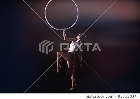 Young woman performing acrobatic element on aerial ring indoors 95318034