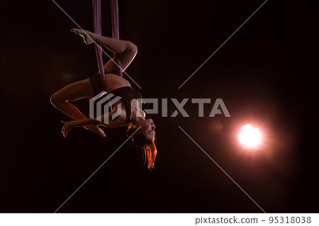 Young woman performing acrobatic element on aerial silk against dark background. Space for text 95318038