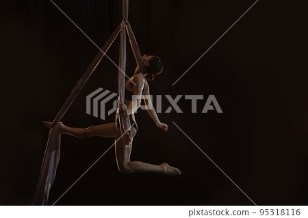 Young woman performing acrobatic element on aerial silk indoors. Space for text 95318116