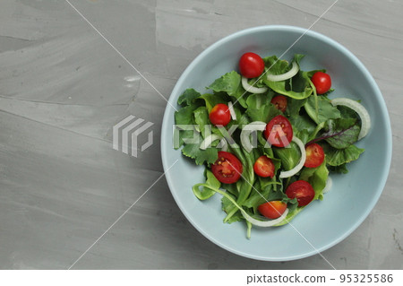 arugula salad of cherry tomato iceberg and sweet onions with a dressing in a setlo blue plate on a gray background with space for text. Healthy delicious food vegetables vitamins 95325586