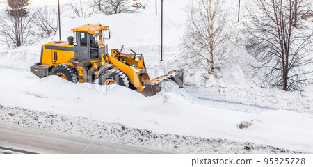 Snow clearing. Tractor clears the way after heavy snowfall. A large orange tractor removes snow from the road and clears the sidewalk. Cleaning roads in the city from snow in winter. Snow clearing. Tractor clears the way after heavy snowfall. A large orange tractor removes snow from the road and clears the sidewalk. Cleaning roads in the city from snow in winter. 95325728