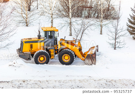Snow clearing. Tractor clears the way after heavy snowfall. A large orange tractor removes snow from the road and clears the sidewalk. Cleaning roads in the city from snow in winter. Snow clearing. Tractor clears the way after heavy snowfall. A large orange tractor removes snow from the road and clears the sidewalk. Cleaning roads in the city from snow in winter. 95325737