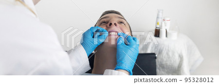 Installation of braces, bridges and a dental plate to correct teeth. An orthodontist installs a bracket system on an uneven jaw. Implants and smile correction. Concept of working in the dentist office Installation of braces, bridges and a dental plate to correct teeth. An orthodontist installs a bracket system on an uneven jaw. Implants and smile correction. Concept of working in the dentist office 95328012