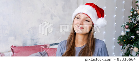 Young woman in blue pajamas and santa claus hat in decorated bedroom interior Young woman in blue pajamas and santa claus hat in decorated bedroom interior 95330664