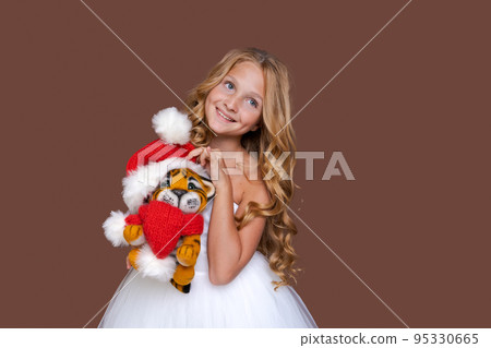 Child plays with cute little Christmas tiger toy in white dress on brown Child plays with cute little Christmas tiger toy in white dress on brown 95330665