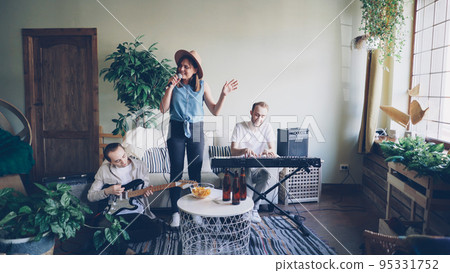 Pretty blonde vocalist from popular musical band is singing and dancing while her friends guitarist and keyboarder are playing guitar and keyboard and smiling. 95331752