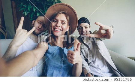 Point of view shot of creative funny friends holding camera and taking selfie, posing and gesturing, smiling and laughing. Friendship and happy young people concept. 95331796