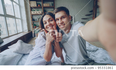 Point of view shot of happy couple famous bloggers recording video for their followers at home. Young people are talking and gesturing looking at camera. 95331861