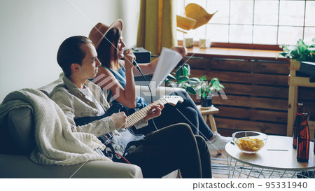 Creative musical duet is practising at home attractive woman is singing in microphone and handsome man is playing the guitar. Young cheerful people are wearing casual clothes. Creative musical duet is practising at home attractive woman is singing in microphone and handsome man is playing the guitar. Young cheerful people are wearing casual clothes. 95331940