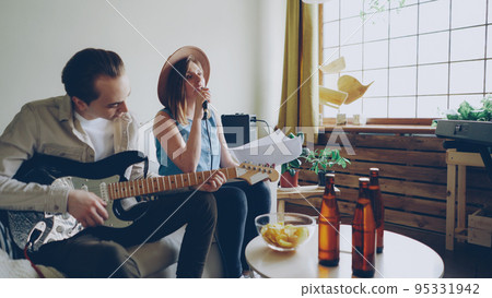 Creative musical duet is practising at home attractive woman is singing in microphone and handsome man is playing the guitar. Young cheerful people are wearing casual clothes. Creative musical duet is practising at home attractive woman is singing in microphone and handsome man is playing the guitar. Young cheerful people are wearing casual clothes. 95331942