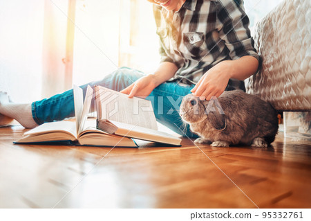 A happy young woman sits on the floor and shows a book to a rabbit. Side view. Concept of reading and education A happy young woman sits on the floor and shows a book to a rabbit. Side view. Concept of reading and education 95332761