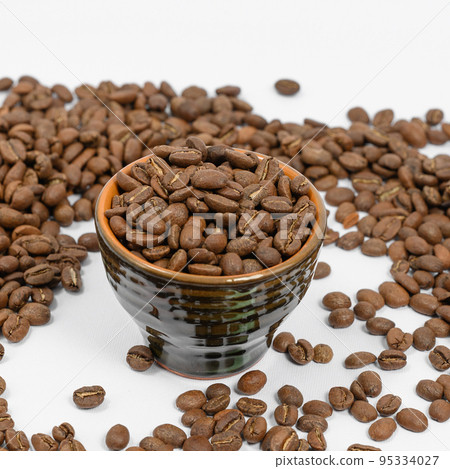 Fragrant roasted coffee beans on a white background and a small cup. Fragrant roasted coffee beans on a white background and a small cup. 95334027