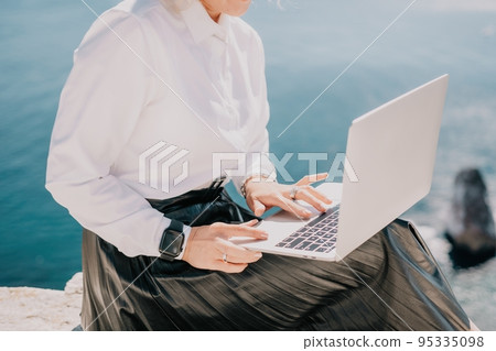 Digital nomad, Business woman working on laptop by the sea. Pretty lady typing on computer by the sea at sunset, makes a business transaction online from a distance. Freelance, remote work on vacation Digital nomad, Business woman working on laptop by the sea. Pretty lady typing on computer by the sea at sunset, makes a business transaction online from a distance. Freelance, remote work on vacation 95335098