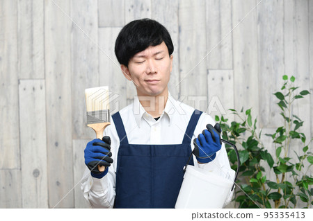 A young man in an apron who is in trouble while holding a brush A young man in an apron who is in trouble while holding a brush 95335413