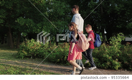 happy family. father leads children by hand school. boy girl child with school backpacks rush lesson. caring dad with his daughter son are walking around school yard. happy family concept. teamwork. 95335664