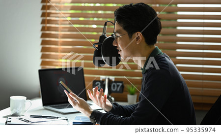 Side view of young asian man recording conversation for her channel to recording podcast in small home studio 95335974