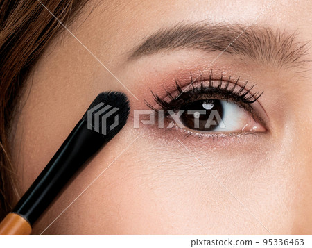 Closeup ardent female model applying her eyeshadow and holding a mirror. 95336463