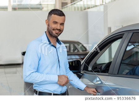 Smiling customer opening the doorknob of his own just bought car at the dealership Smiling customer opening the doorknob of his own just bought car at the dealership 95336676