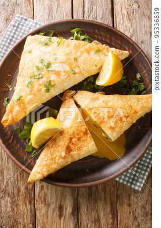 Traditional Tunisian cuisine Brik pastries with tuna and egg srved with lemon close up in the plate. Vertical top view Traditional Tunisian cuisine Brik pastries with tuna and egg srved with lemon close up in the plate. Vertical top view 95336859