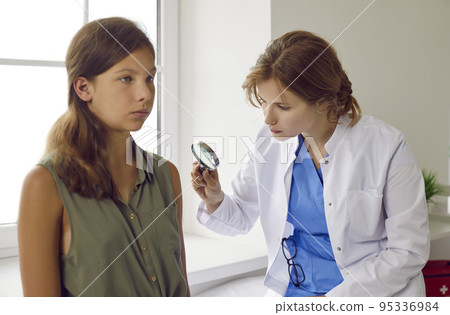 Dermatologist looking through magnifying glass while examining skin of child patient Dermatologist looking through magnifying glass while examining skin of child patient 95336984