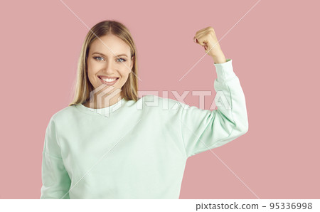 Beautiful smiling woman raises her hand showing her biceps as sign of her strength and confidence. 95336998