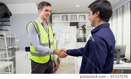An engineer with a protective vest handshake with an investor in his office An engineer with a protective vest handshake with an investor in his office 95337076