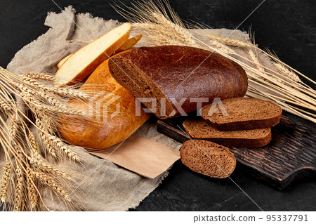 Sliced loaves of white and rye bread with burlap and ears of wheat on black background Sliced loaves of white and rye bread with burlap and ears of wheat on black background 95337791