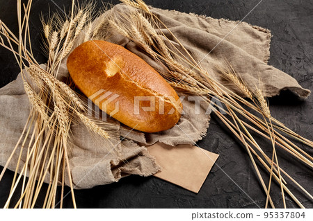 Wheat bread loaf on coarse burlap with ears of wheat on black background Wheat bread loaf on coarse burlap with ears of wheat on black background 95337804