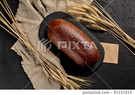 Freshly baked whole rye bread with ears of wheat on black background Freshly baked whole rye bread with ears of wheat on black background 95337814