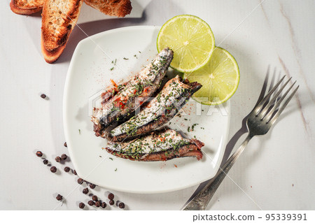 Appetizer of sardines in oil with parsley and paprika on a plate with some toast and lemon slices. 95339391