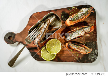 Arrangement of Spanish tapas of sardines in olive oil on toasts on a rustic wooden board and a can of sardines next to the tapas. 95339395