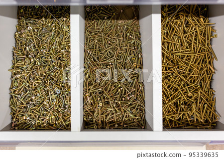 Box with screws of different sizes in a store or workshop. Storage compartments filled with various self-tapping screws for wood. 95339635