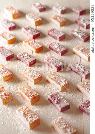 Fruit and berry flavored jelly candies sprinkled with powdered sugar on white wooden table Fruit and berry flavored jelly candies sprinkled with powdered sugar on white wooden table 95339822