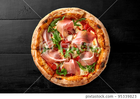 Pizza with pelati sauce, mozzarella, cabanossi, chicken fillet, bacon, prosciutto, arugula on black wooden background Pizza with pelati sauce, mozzarella, cabanossi, chicken fillet, bacon, prosciutto, arugula on black wooden background 95339823