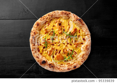 Pizza on thin dough with melted mozzarella, cheddar, chicken fillet and corn on black wooden background Pizza on thin dough with melted mozzarella, cheddar, chicken fillet and corn on black wooden background 95339839