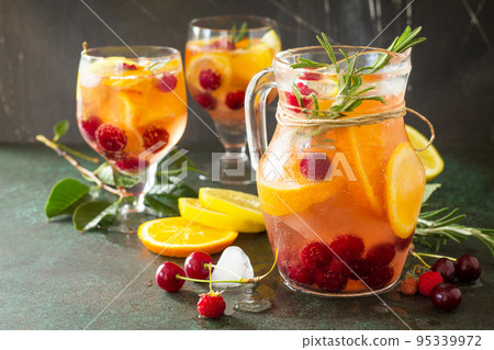Homemade refreshing wine sangria or punch with fruits in glasses. Sangria cocktails with fresh fruits, berries and rosemary. On a stone or slate background, with a jug and ingredients. Copy space. 95339972