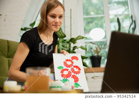 Remote master class of painting. Professional female artist painting floral pattern, ornament on paper, teaching students using laptop at home. Hobby and leisure concept. Remote master class of painting. Professional female artist painting floral pattern, ornament on paper, teaching students using laptop at home. Hobby and leisure concept. 95342514