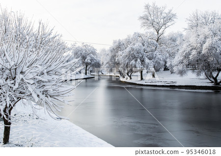 winter park, trees and a bench covered with snow, the river partly covered with ice 95346018