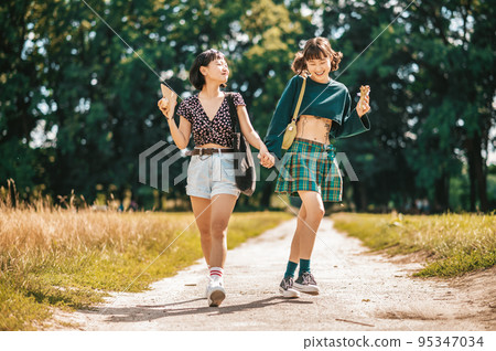 Young pretty girls walking in the park and holding hands Young pretty girls walking in the park and holding hands 95347034