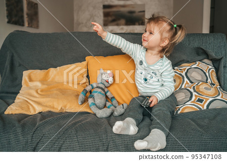 Little girl with a TV accessory sitting on the sofa 95347108
