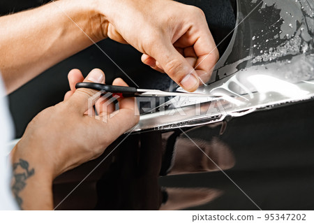 Car wrapping specialist wraps a car with adhesive film in car detailing service 95347202