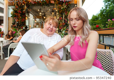 Mother with disability in wheelchair and her daughter using digital tablet while sitting at the table in cafe Mother with disability in wheelchair and her daughter using digital tablet while sitting at the table in cafe 95347240
