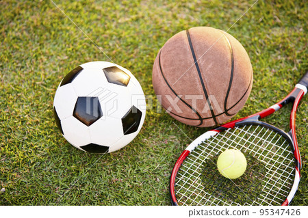 football soccer ball basketball tennis ball and racket laid on grass at sunset, closeup 95347426