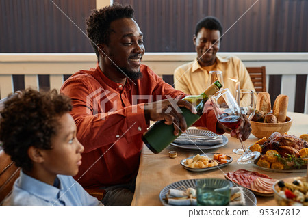 Young Man Pouring Wine at Dinner Table Outdoors Young Man Pouring Wine at Dinner Table Outdoors 95347812
