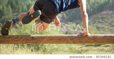 Participant in an obstacle course running, jump over wooden log obstacle 95348182