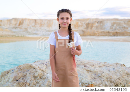 A pretty girl with a long braid on the shore of the lake looks into the distance 95348193