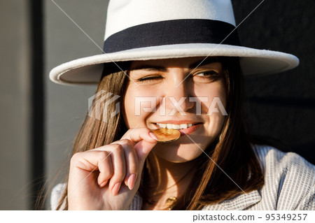 Beautiful brunette girl checks bitcoin for authenticity with the help her teeth. Bitcoin concept 95349257