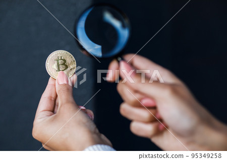 Close up of female hand holding magnifying glass and looking through it at bitcoin. The concept of research and study of the cryptocurrency market 95349258