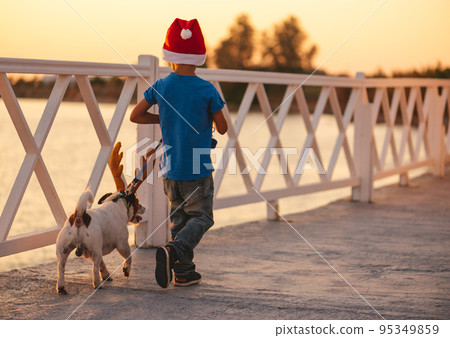 Holidays at beach concept with child and dog wearing Christmas and New Year costumes at seafront Holidays at beach concept with child and dog wearing Christmas and New Year costumes at seafront 95349859