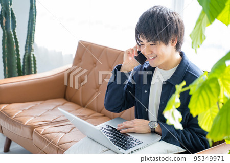 Men in their 20s working on a computer and smartphone-living sofa and foliage plants Men in their 20s working on a computer and smartphone-living sofa and foliage plants 95349971